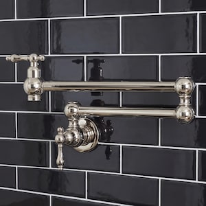 Puede incluir: Un grifo de llenado de ollas montado en la pared de níquel pulido con un brazo articulado de doble articulación y dos manijas de palanca. El grifo tiene un acabado metálico reflectante y está montado contra una pared de azulejos negros brillantes.