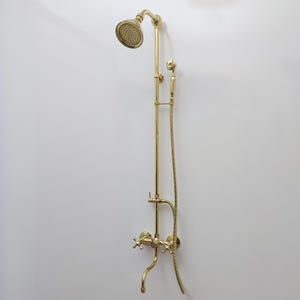 May include: A gold-toned shower head and faucet set with a handheld shower head and a diverter valve. The shower head is attached to a long, vertical pipe.