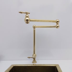 May include: A gold-toned kitchen tap with a swivel spout and a single handle. The tap is mounted on a worktop and has a polished finish.