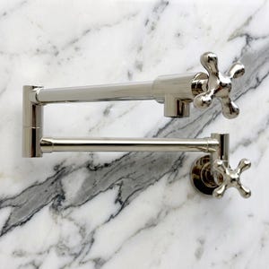 Può includere: Un rubinetto a parete per riempire pentole in nichel lucido, dotato di un braccio articolato a doppio snodo e due manopole a croce. L'accessorio presenta una finitura metallica riflettente e un design a più sezioni per la massima estensione.