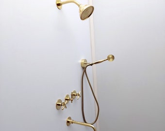 May include: A gold shower head with a handheld shower head and a shower arm. The shower head is mounted on a white wall.