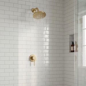 May include: A brushed gold shower head and a matching single-handle mixing valve mounted on a white subway tile wall. Water flows from the circular shower head, and a recessed niche contains two bottles of liquid soap within the shower enclosure.