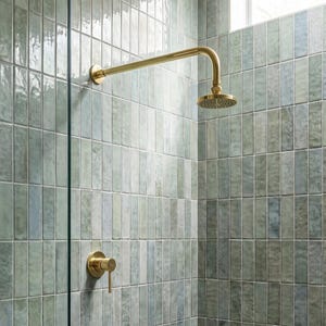 May include: A brass shower head and matching single-handle control valve mounted on a wall covered in vertical, rectangular, light green and blue glazed ceramic tiles with a glossy finish and subtle colour variations throughout the surface.