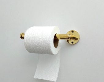 May include: A gold-toned toilet paper holder with a roll of white toilet paper. The holder is mounted to a white wall.