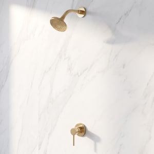May include: A brushed gold shower head and a matching single-handle shower control valve mounted on a white marble wall with grey veining. The shower head is circular with multiple small water outlets, and the handle is a cylindrical lever.