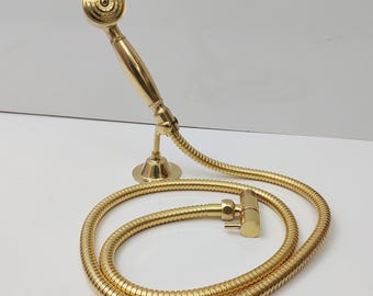 Op de afbeelding: Een gouden handdouche met een flexibele slang. De douchekop heeft een ronde, platte sproeikop met meerdere gaten. De slang is opgerold en heeft een messingkleurige connector.
