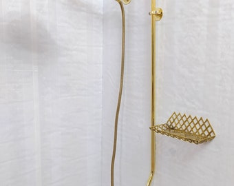 May include: A gold-colored shower fixture with a round showerhead and a handheld showerhead. The fixture includes a soap dish and faucet controls. The showerhead is mounted on a curved arm. The fixture is mounted on a white wall.