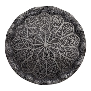 May include: A detailed, circular metal tray with an intricate, symmetrical pattern. The tray's surface is etched with floral and geometric designs, radiating from a central point. The tray has a dark, antique finish, and a decorative border.