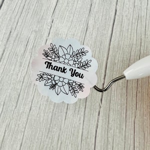 May include: White round sticker with a black floral design and the text "Thank You".