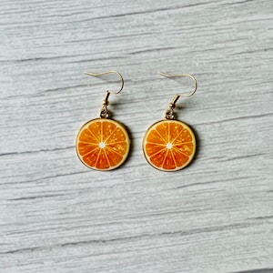 May include: A pair of gold earrings with orange slice charms. The earrings are a fun and trendy accessory for any occasion.