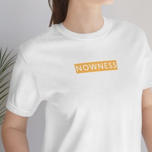 May include: White t-shirt with a yellow rectangle and the word "NOWNESS" printed in white.