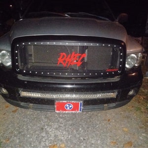 May include: A black pickup truck with a black mesh grille and a red "RARE" logo. The truck has a silver hood and a Tennessee license plate.