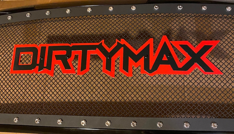 Puede incluir: Una parrilla de metal negro con un logotipo "DIRTYMAX" rojo y negro. La parrilla est&aacute; hecha de un material de malla y tiene un marco negro.