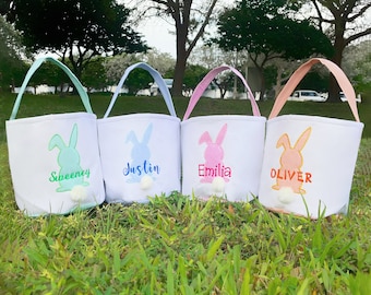 May include: Four white Easter baskets with bunny ears and pom-poms. The baskets are personalized with the names "Sweeney", "Justin", "Emilia", and "Oliver".