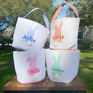 May include: Four white Easter baskets with bunny silhouettes and personalized names. The baskets are lined with pink, blue, green, and orange gingham fabric. The bunnies have fluffy white tails.