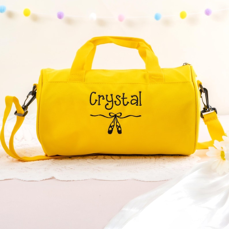 Pu&ograve; includere: Borsa da viaggio in tela gialla con un design ricamato nero di scarpe da balletto e il nome "Crystal".