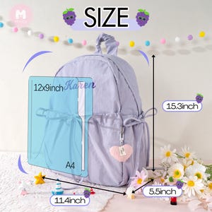May include: A lavender backpack with a front pocket and a small heart-shaped charm. The backpack measures 15.3 inches high, 12 x 9 inches wide, and 5.5 inches deep. The text "Karen" is visible on the front pocket. The backpack is next to a bouquet of flowers.
