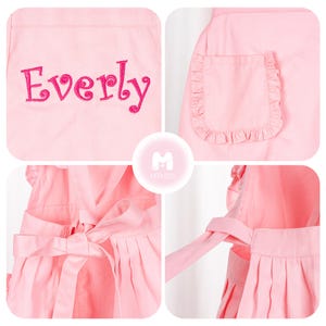 May include: Pink child's apron with a frilled pocket and adjustable straps. The apron has the name "Everly" embroidered on the front.