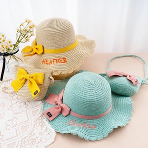 May include: A collection of straw hats and matching purses. One hat is beige with a yellow band and bow, the name "HEATHER" embroidered in orange. Another is light blue with a pink band and bow, the name "Sophia" embroidered in pink.