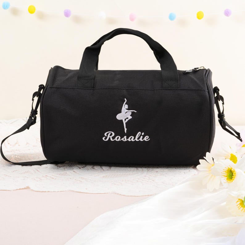 Pu&ograve; includere: Borsa da viaggio in tela nera con una ballerina ricamata in bianco e il nome "Rosalie".