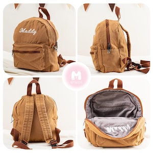 K&ouml;nnte beinhalten: Ein brauner Canvas-Rucksack mit verstellbaren Tr&auml;gern. Der Rucksack hat eine Rei&szlig;verschlusstasche vorne und ein gro&szlig;es Hauptfach. Der Rucksack ist mit dem Namen "Maddy" in wei&szlig;er Stickerei personalisiert.