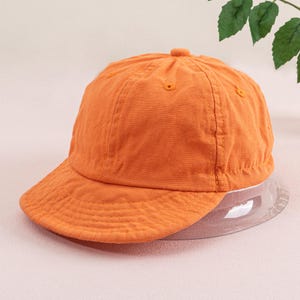 May include: A bright orange baseball cap with a curved brim. The cap is made of a soft, textured fabric.