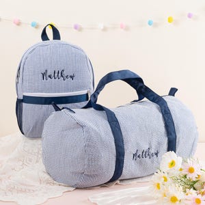 May include: Blue and white striped personalized duffel bag and backpack set with the name "Matthew" embroidered on each.