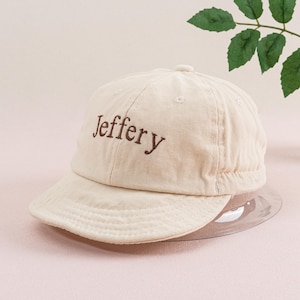 May include: A beige baseball cap with a brown embroidered name "Jeffery" on the front.