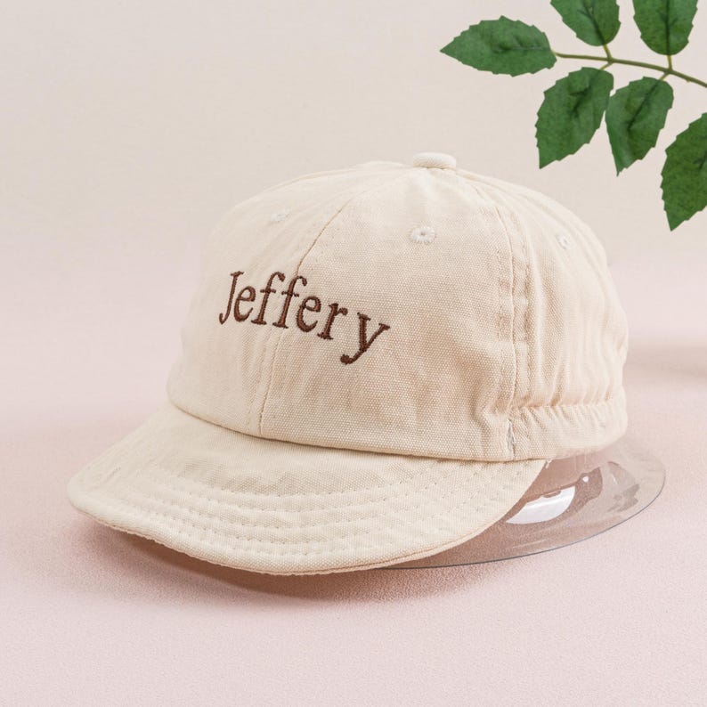 May include: A beige baseball cap with a brown embroidered name "Jeffery" on the front.