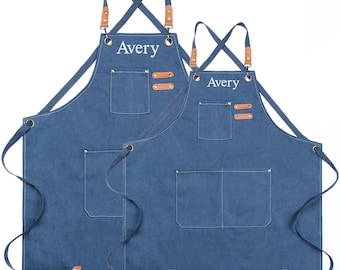 Può includere: Due grembiuli in denim blu con spalline regolabili e una grande tasca. I grembiuli sono personalizzati con il nome "Avery" in ricamo bianco.