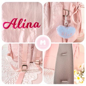 May include: Pink backpack with the name "Alina" embroidered in a cursive font. The backpack has adjustable straps, a mesh back panel, and a heart-shaped keychain. The backpack is made of a lightweight, possibly nylon, material.