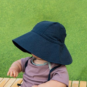 May include: A black sun hat with a wide brim, worn by a child sitting on a wooden surface.