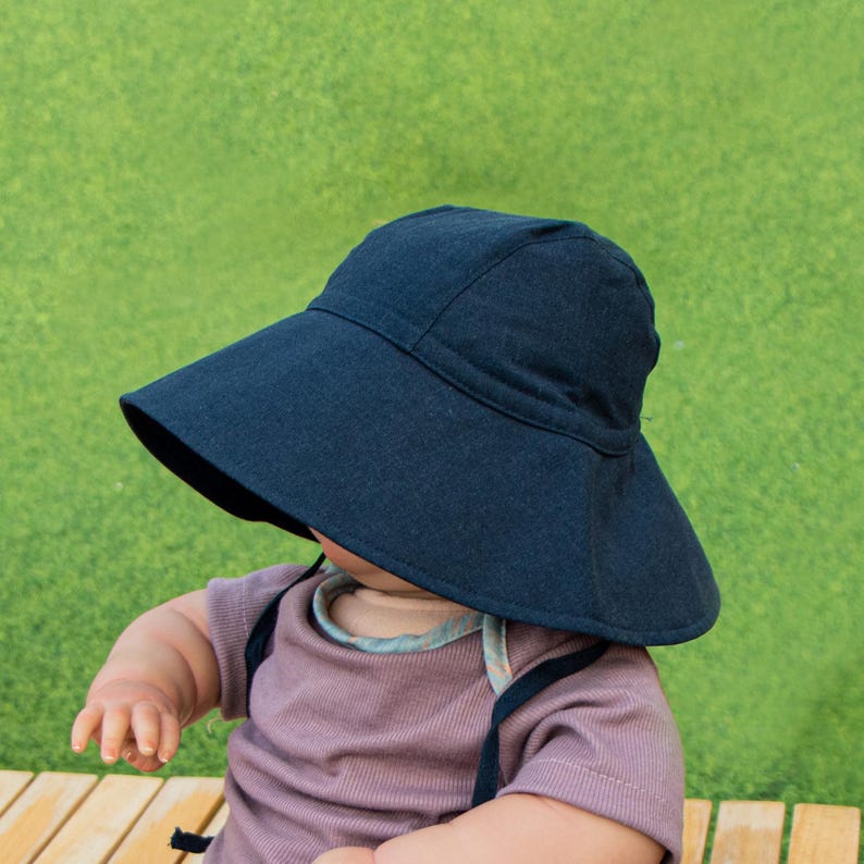 May include: A black sun hat with a wide brim, worn by a child sitting on a wooden surface.