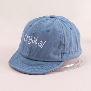 May include: A blue baseball cap with a white embroidered word "Crystal" on the front.