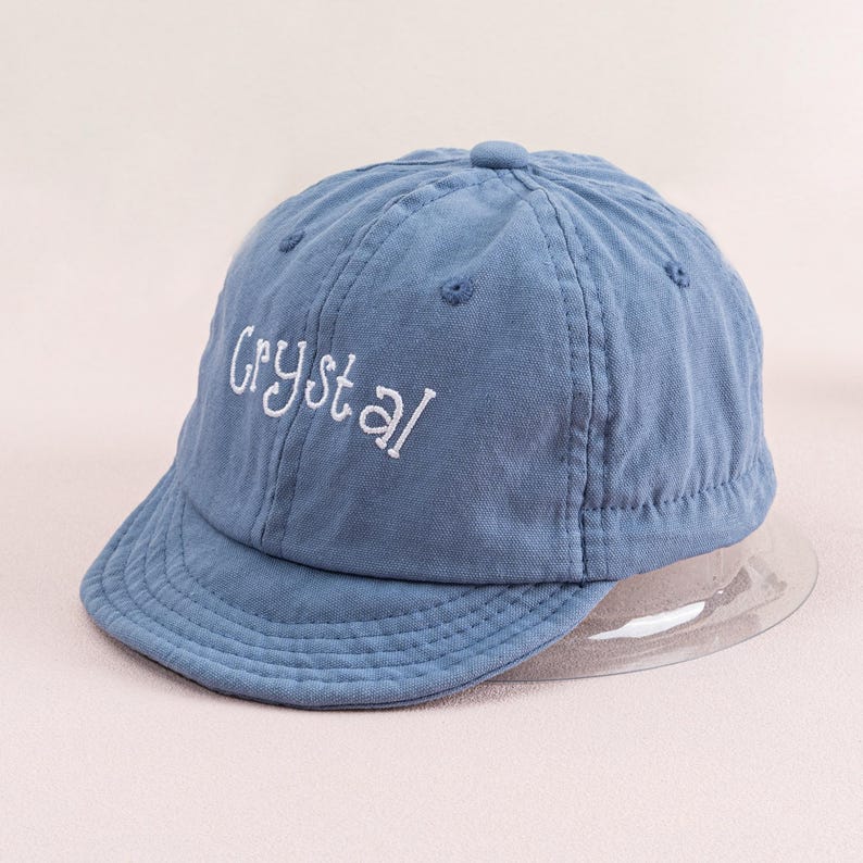 May include: A blue baseball cap with a white embroidered word "Crystal" on the front.