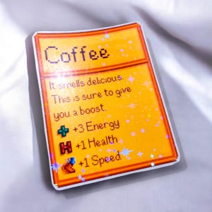 May include: A rectangular sticker with a yellow background and the word "Coffee" at the top. The sticker includes text that reads "It smells delicious. This is sure to give you a boost. +3 Energy, +1 Health, +1 Speed."