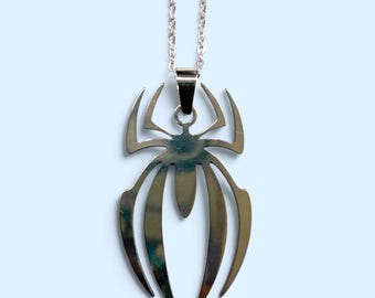 Pode incluir: Um pingente de metal prateado em forma de aranha estilizada com pernas alongadas e pontiagudas, suspenso por uma corrente de elos a condizer. O design apresenta uma superfície lisa e refletora com uma silhueta simétrica de bordos afiados.