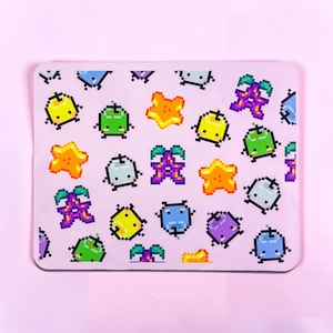 May include: A rectangular mouse pad with a light pink background featuring a repeating pixel art pattern of various colorful fruits and star shapes, including green apples, yellow apples, purple grapes, and orange stars with small facial features.