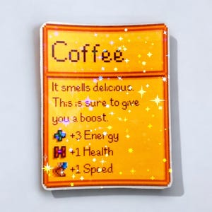 May include: A rectangular sticker with a yellow background and a brown border. The word "Coffee" is at the top. Below, text reads "It smells delicious. This is sure to give you a boost." with game stats: +3 Energy, +1 Health, and +1 Speed.