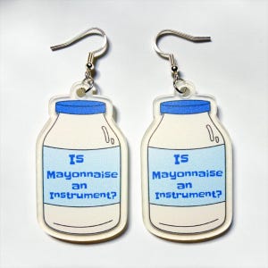 May include: A pair of dangle earrings featuring a flat, translucent acrylic charm shaped like a jar of mayonnaise. The jar has a blue lid and a blue label with the text 'Is Mayonnaise an Instrument?' printed in a bold, blue, blocky font.