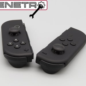 Könnte beinhalten: Zwei schwarze Nintendo Switch Joy-Con-Controller mit schwarzen Analogsticks und Knöpfen. Die Controller sind getrennt und auf einer weißen Oberfläche positioniert.
