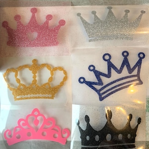 May include: Six crown-shaped iron-on transfers arranged in a grid. The top left is pink glitter, top right is silver glitter, middle left is gold glitter, middle right is blue glitter, bottom left is solid neon pink, and bottom right is black glitter.