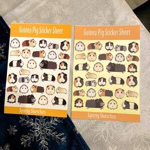May include: Two sheets of stickers featuring adorable guinea pigs in various poses. Each sheet has the title "Guinea Pig Sticker Sheet" and "Spotty Sketches" at the bottom. The stickers are on a yellow background with a white border.