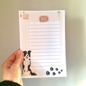 May include: A white notepad with black lines and a black border. The notepad has a brown and white illustration of a dog with black paw prints at the bottom. The notepad has the word "NOTES" in a brown rectangle at the top.