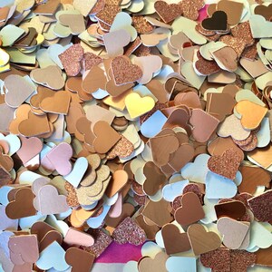 May include: A large pile of rose gold and white heart confetti. The hearts are made of paper and glitter.
