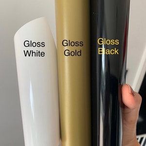 Op de afbeelding: Drie rollen vinyl-plakfolie in glanzend wit, glanzend goud en glanzend zwart.
