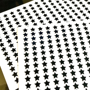 Op de afbeelding: Twee vellen wit papier met zwarte ster stickers. De sterren zijn gerangschikt in rijen en kolommen.
