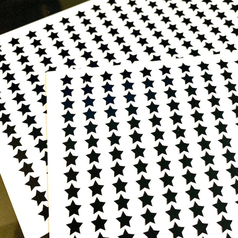 Op de afbeelding: Twee vellen wit papier met zwarte ster stickers. De sterren zijn gerangschikt in rijen en kolommen.