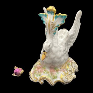 May include: A white porcelain swan figurine with gold and teal accents. The swan is perched on a base with floral details and gold trim.