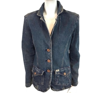 May include: A medium-wash denim blazer with a classic collar and three brown buttons. The blazer has two front pockets with button closures and a small label on the right pocket. The jacket is displayed on a white mannequin.